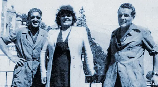 Trois personnes posent devant un paysage. L'homme de gauche, peut-être le fondateur Millet, sourit.