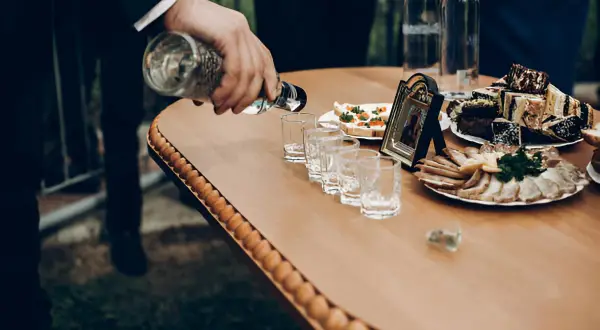 Na weselu nalewana jest wódka do kieliszków. Obok stoją zakąski i tort. Ile wódki na wesele?