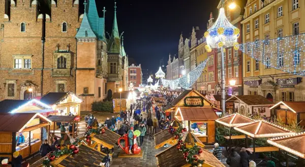 Tłoczny, rozświetlony jarmark bożonarodzeniowy, największy jarmark bożonarodzeniowy w Polsce, z kramami i ludźmi w nocnej scenerii.