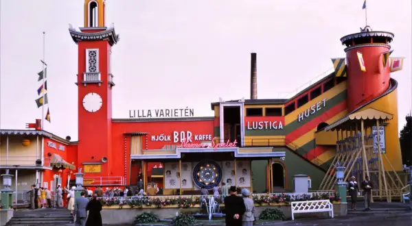 Färgglatt lustiga huset med torn och rutschkana. Folk minglar vid bar och kaffe.