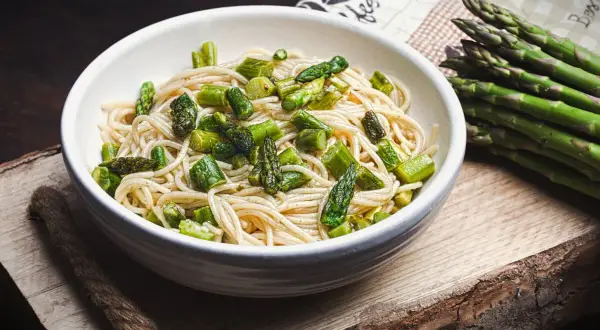Spargel Pasta: Ein Teller Spaghetti mit frischem, grünem Spargel, daneben ein Bund Spargel.
