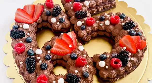 Una torta numero cioccolato, decorata con fragole, lamponi, mirtilli e more.
