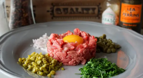 Un plat de tartare de boeuf frais, garni d'un jaune d'oeuf, avec des câpres, des cornichons hachés, des échalotes et du persil.
