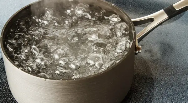 Une casserole en métal sur une plaque de cuisson, l'eau est en train de bouillir avec des bulles et de la vapeur.