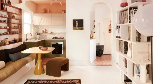 Acogedora casa pequena con cocina verde, sofá cama, mesa amarilla y estanterías llenas de objetos.