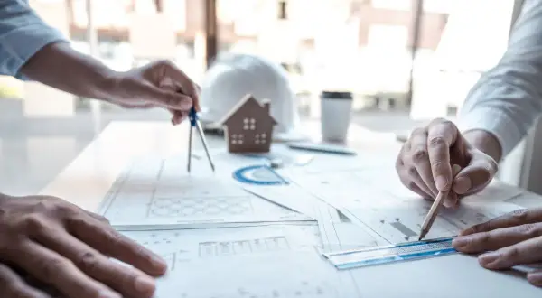 Architetti al lavoro su progetti edilizi, tra cui quelli che rientrano nella CILA. Si vedono mani che usano compasso, matita e righello sui disegni.