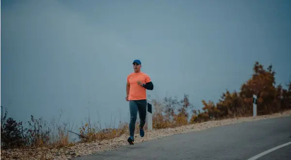 Mężczyzna w pomarańczowej koszulce i czapce biega po pustej drodze. Czy można biegać na czczo? To pytanie zadaje sobie wielu sportowców.