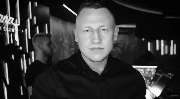 DJ Iroon w czerni, gotowy do rozkręcenia imprezy. W tle neonowe światła klubu.