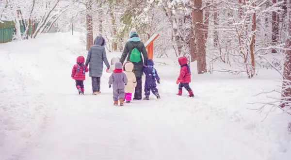 Schneebedeckter Weg im Wald. Eine Gruppe Kinder und eine Erzieherin gehen zum Kindergarten.