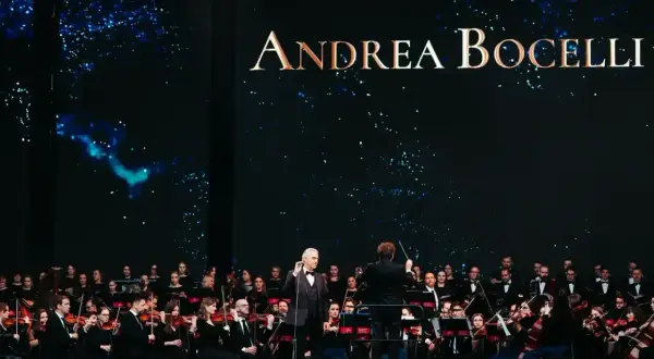 Andrea Bocelli koncert 2026. Wokalista śpiewa z orkiestrą symfoniczną na tle gwieździstego nieba.