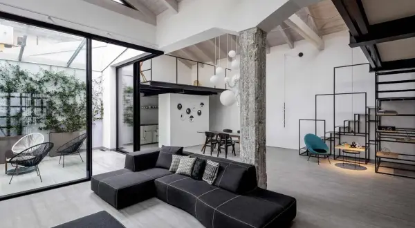 Un ampio soggiorno con tetto a vista e un soppalco, che mostra cos'è un loft: spazio aperto, design industriale e un tocco di verde da un patio interno.