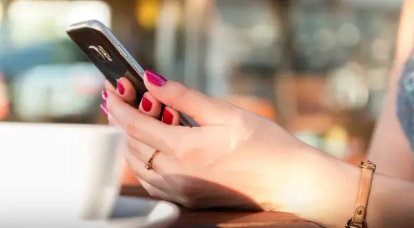 Kobieta z pomalowanymi paznokciami trzyma telefon, szukając informacji, jak zmienić dźwięk powiadomień w Messengerze.
