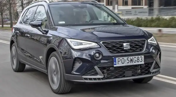 Ciemnoniebieski Seat Arona w ruchu miejskim. Kierowca w okularach. Wiele pozytywnych seat arona opinie potwierdza jego miejski charakter.