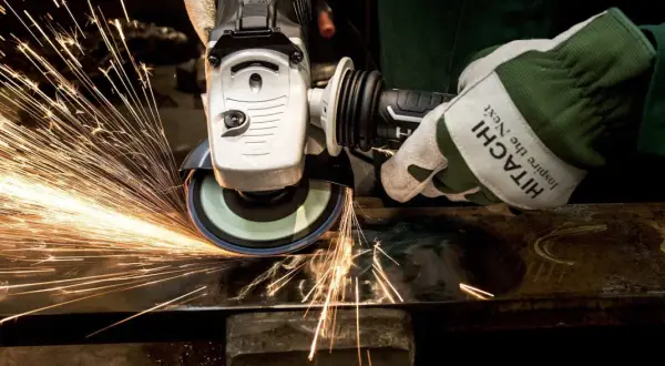 Ręka w rękawicy Hitachi szlifuje metal, tworząc deszcz iskier. To przykład działania siły tarcia statycznego.