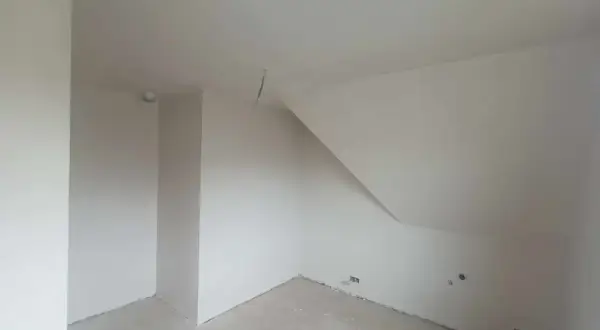 Wnętrze pokoju ze skośnym sufitem, ściany pokryte tynkiem gipsowym bez gładzi, gotowe do malowania.