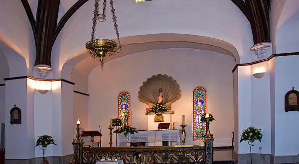 Interior de la iglesia de conchas Galicia, con altar, vitrales y lámpara colgante.