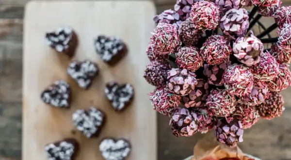En bukett med rosa och lila cake pops, dekorerade med strössel och hjärtan. Bredvid ligger mörka hjärtformade cake pops.