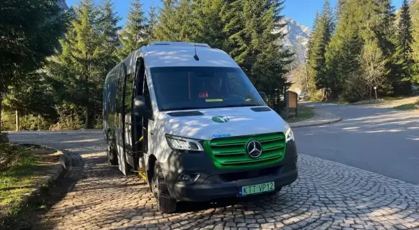 Nowy, ekologiczny bus na Morskie Oko czeka na turystów. W tle góry i las.