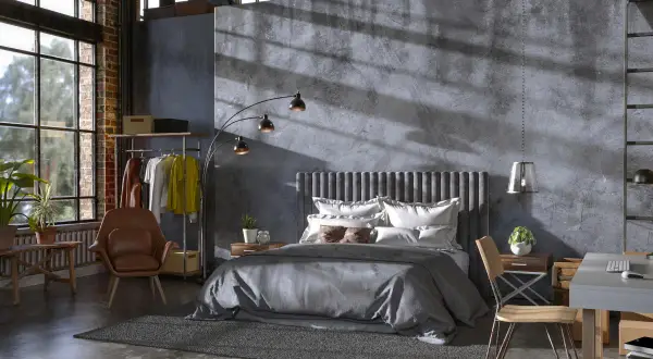 Przytulny soft loft z łóżkiem, fotelem i biurkiem. Duże okna wpuszczają światło, podkreślając surowy charakter wnętrza.