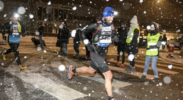 Coureurs de la SaintéLyon affrontant la neige. Un homme porte une lampe frontale et un dossard "Asics".