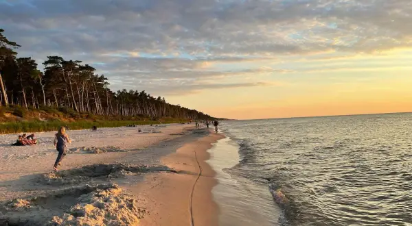 Piękny zachód słońca na plaży w Choczewie. Ludzie spacerują, a morze delikatnie faluje.