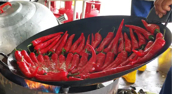 Viele rote Chilis brutzeln in einer Pfanne über offenem Feuer. Wenn der Chili zu scharf ist, was tun? Vielleicht mehr Öl hinzufügen?