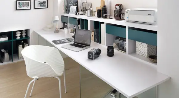 Un moderno despacho en buhardilla con un portátil, cámaras, impresora y una silla blanca.