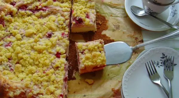 Pyszne ciasto drożdżowe z budyniem i owocami, posypane kruszonką. Gotowe do podania na talerzykach z widelcami.