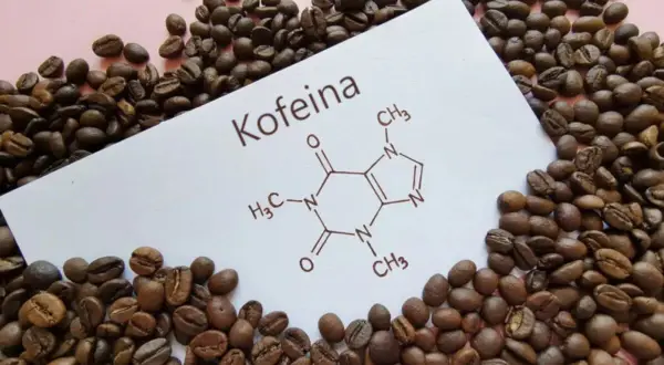 Ziarna kawy otaczają kartkę z napisem "Kofeina" i jej wzorem chemicznym. Czy kofeina w tabletkach jest zdrowa?