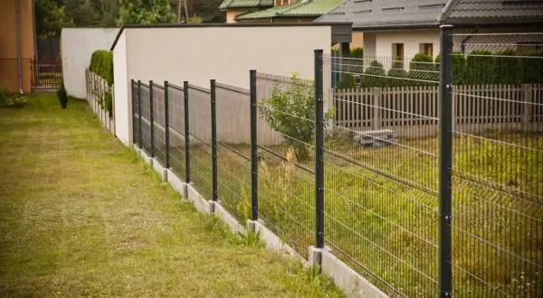 Nowoczesne ogrodzenie działki z siatki i paneli, biegnące wzdłuż trawnika i domów.