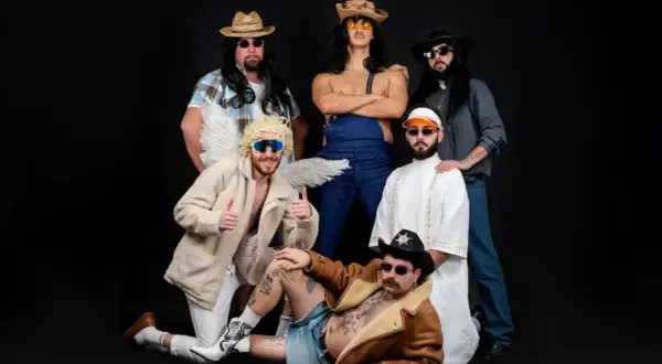 Un gruppo di amici, tra cui un angelo con ali e un cowboy, posa per una foto. Sembrano un gruppo di "ken la fen" pronti per una festa.