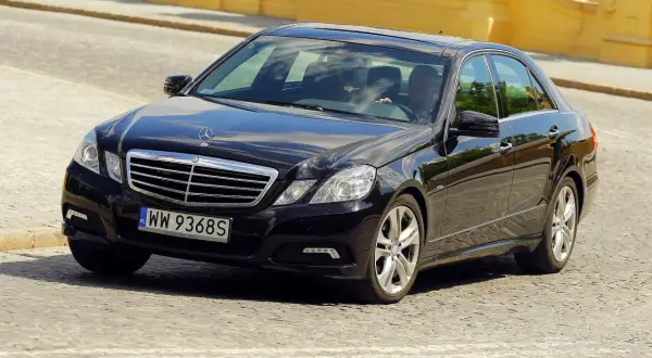 Elegancki, czarny Mercedes-Benz Klasa E porusza się po brukowanej ulicy.