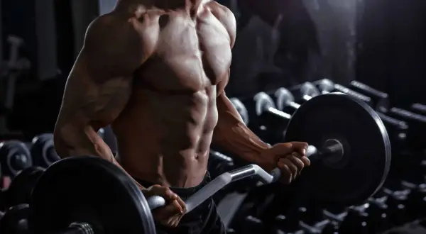 Uomo muscoloso in palestra esegue curl con bilanciere. Quante serie per gruppo muscolare sono necessarie per ottenere un fisico scolpito come questo?