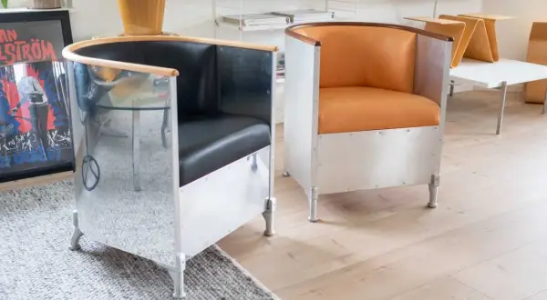 Två fåtöljer i källemo aluminium med svarta och orange lädersitsar. En spegelblank yta reflekterar rummet.