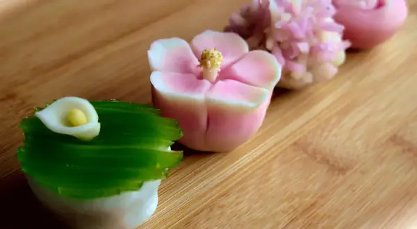 Délicates pâtisseries japonaises en forme de fleurs et de calla, aux couleurs pastel, sur fond de bois.