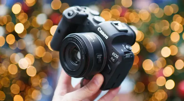 Dłoń trzyma aparat Canon EOS R6 z obiektywem 50 mm f/1.8 STM na tle świątecznych światełek.