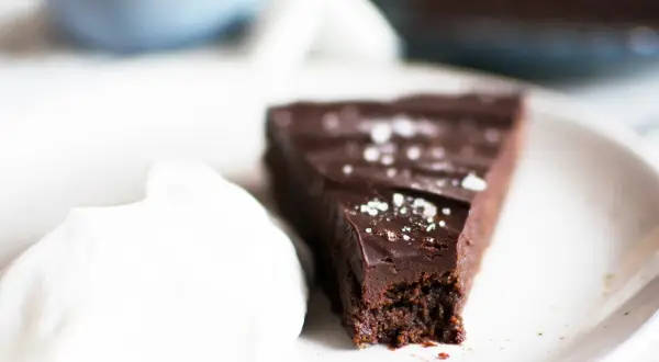 En bit vegansk kladdkaka med en klick vispad grädde, strödd med flingsalt.