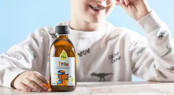 Chłopiec je tran z łyżeczki. Obok stoi butelka z płynnym tranem.