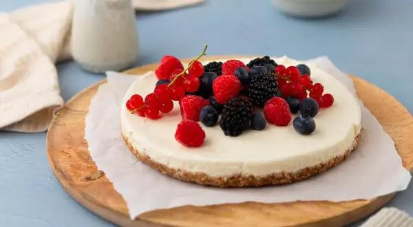 Kalter Hund: Ein cremiger Käsekuchen mit Beeren-Topping, serviert auf einem Holzbrett.