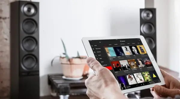 Mann sucht auf einem Tablet nach neue Musik. Im Hintergrund stehen zwei schwarze Lautsprecher.