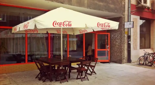 Tanie jedzenie Wrocław Rynek: stoliki pod parasolem Coca-Cola, wejście do lokalu, rowery przy ścianie.