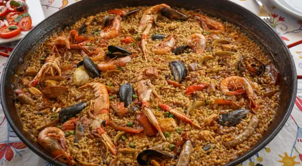 Une paella valenciana généreuse, débordant de riz, crevettes, moules et langoustines, prête à être dégustée.