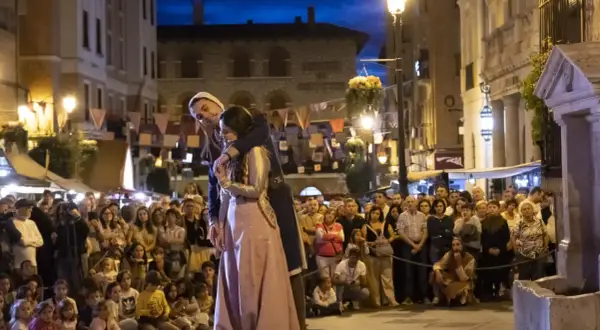 Una pareja se abraza en una calle iluminada por farolas, ante una multitud que observa. Podría ser la escena de "la partida de Diego".