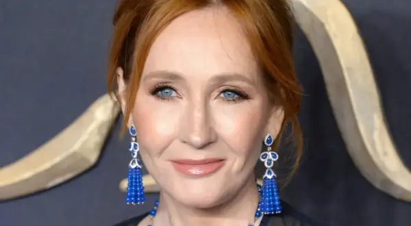 J.K. Rowling, która stworzyła postać Harry'ego Pottera, z niebieskimi oczami i rudymi włosami, w eleganckich, niebieskich kolczykach.