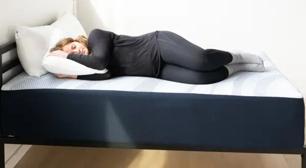 A woman sleeps soundly on a dark blue mattress, experiencing the comfort of one of the mejores colchones para dormir en Estados Unidos.