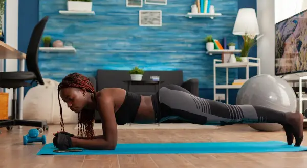 Donna esegue esercizi addominali bassi in posizione di plank su un tappetino blu, concentrata sul suo allenamento casalingo.