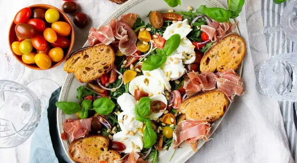 En härlig buffé med appertiff mat: mozzarella, tomater, prosciutto, ruccola och rostat bröd. Perfekt för en somrig förrätt.