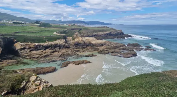 Senderistas disfrutan de las impresionantes rutas senderismo Foz, con acantilados rocosos, playas de arena y el mar azul.