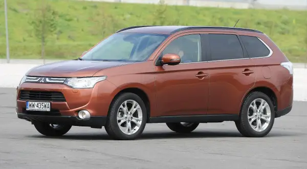 Brązowy Mitsubishi Outlander 3 na tle zielonego wzgórza.