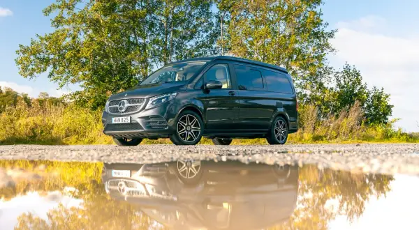 Mörkgrå Mercedes-Benz Vito med takhöjning, perfekt för service och äventyr. Reflekteras i en vattenpöl.